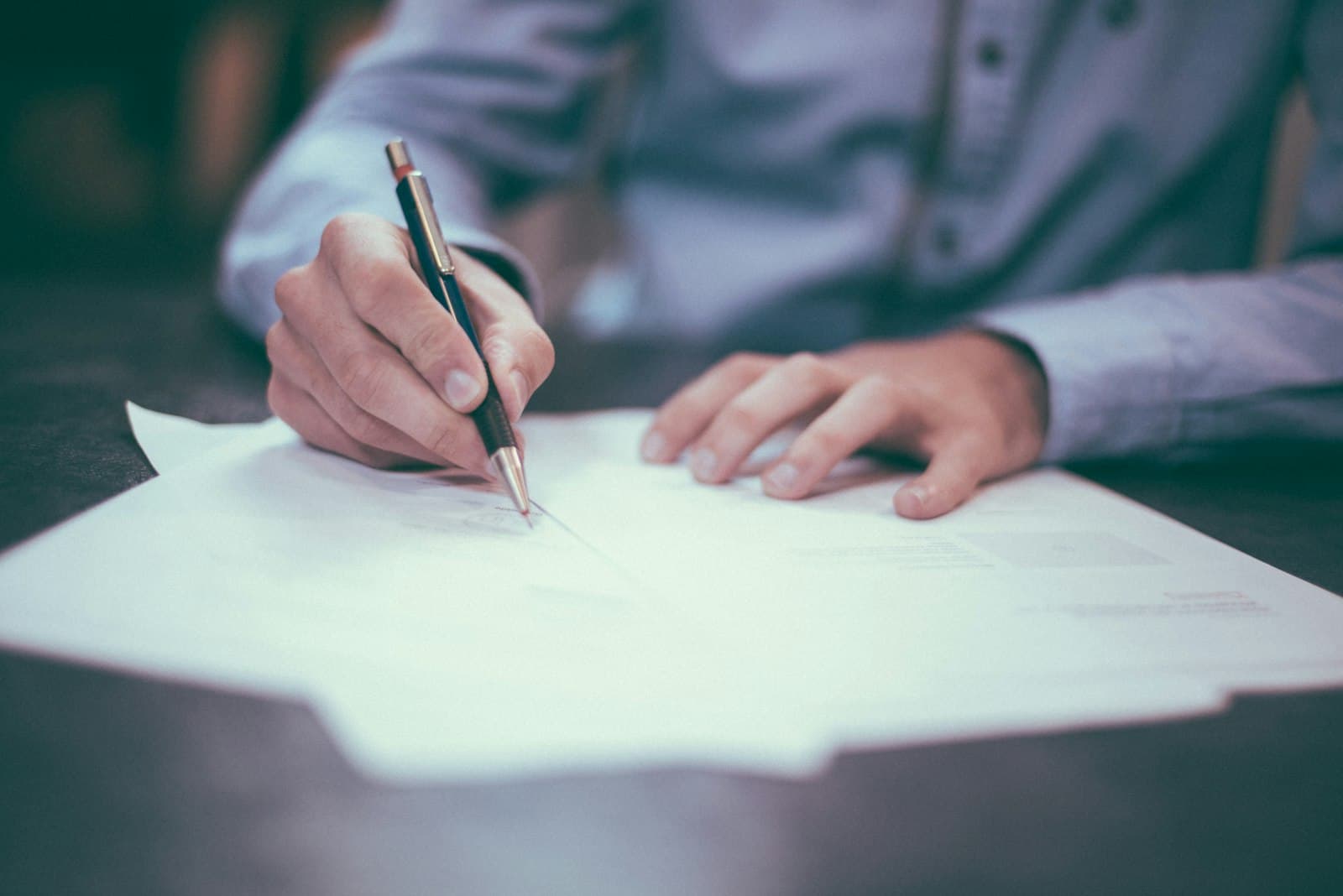 Mão assinando um documento sobre a mesa de um escritório